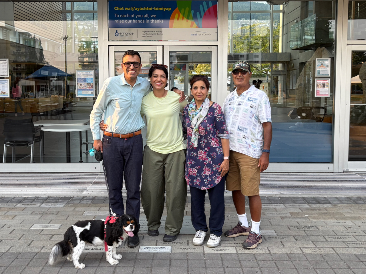 Jay Sidhu and three supporters, with a small dog, standing outside the West Vancouver Community Centre beneath a welcome banner